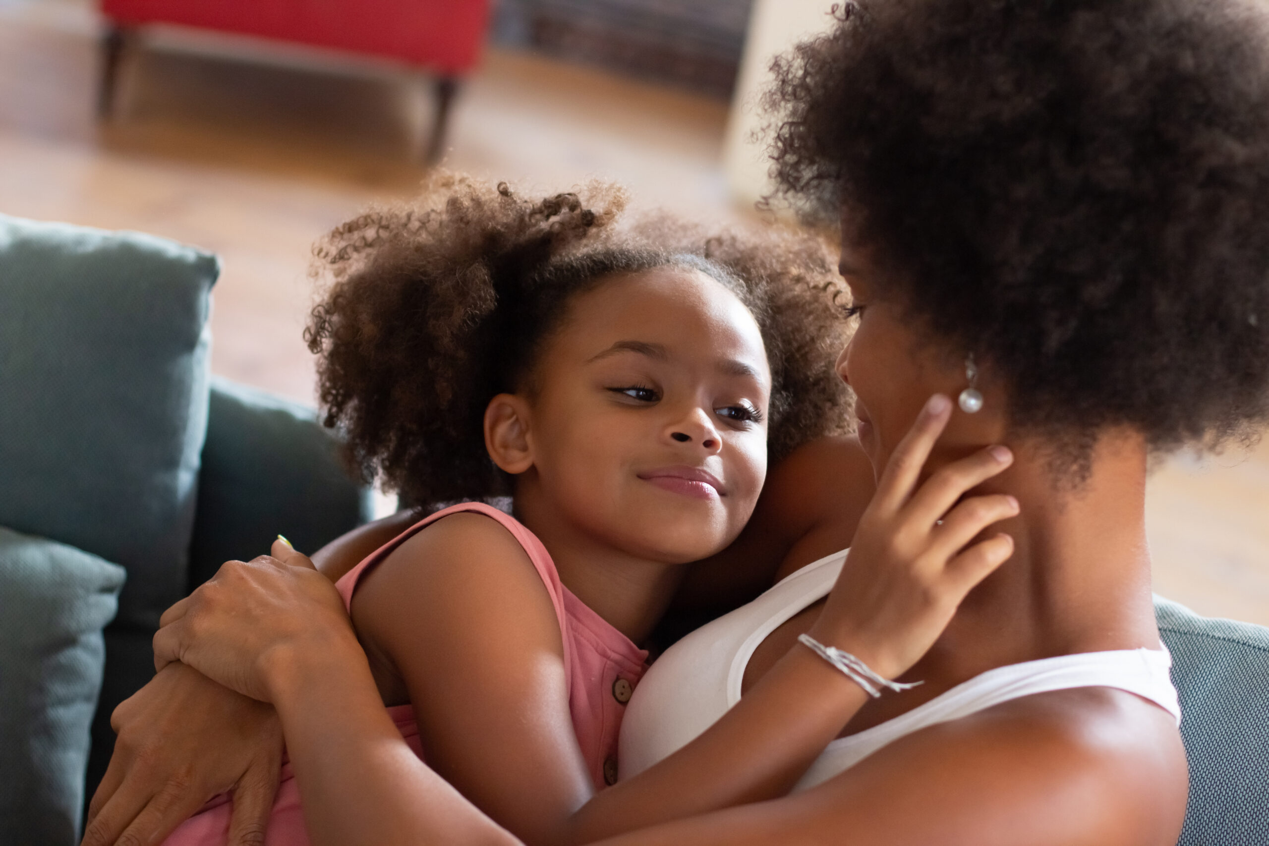Loving African American mother and daughter hugging. Woman and girl in casual clothes holding each other on coach. Love, family, bonding concept